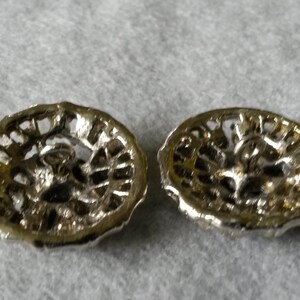 May include: Two silver-toned, filigree-style buttons with a floral design. The buttons have a circular shape with a detailed openwork pattern. The backs of the buttons are visible, showing the attachment loops.
