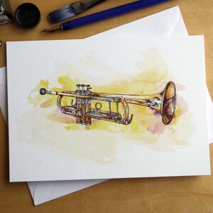 Könnte beinhalten: Aquarellillustration einer Trompete auf einer weißen Karte. Das Blechblasinstrument ist detailliert mit einer gelb-braunen Farbpalette dargestellt, vor einem weichen Aquarellhintergrund. Tintenfässer und ein Pinsel sind sichtbar.