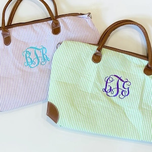 May include: Two striped tote bags with leather handles. The bag on the left is lavender and white with a turquoise monogram "BJR". The bag on the right is green and white with a purple monogram "DJS".