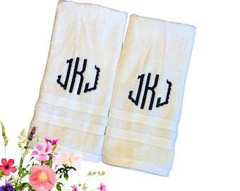 May include: Two white terry cloth hand towels featuring a dark navy blue embroidered monogram of the letters JK in a decorative script font. Each towel has a textured border with three horizontal lines near the bottom edge of the fabric.