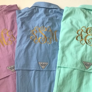 May include: Three button-down shirts with embroidered monograms. The shirts are in shades of pink, blue, and green. Each shirt has a small logo patch on the back.