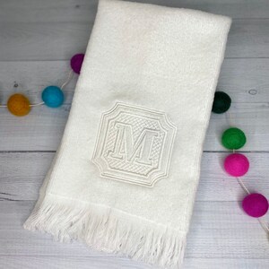 May include: White hand towel with a fringed edge and an embroidered letter "M" in a decorative frame.