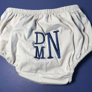 May include: White cotton baby bloomers with blue embroidered initials "DNM".