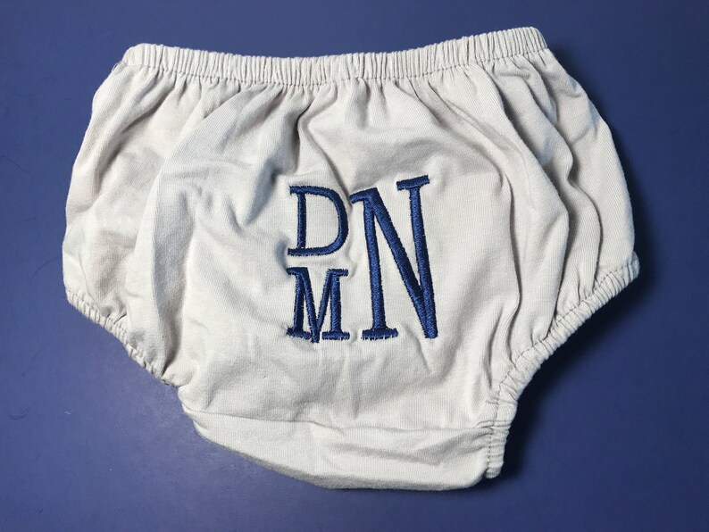 May include: White cotton baby bloomers with blue embroidered initials "DNM".