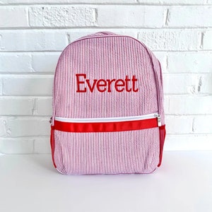 May include: Pink and white striped backpack with a red zipper and red trim. The backpack is personalized with the name "Everett" in red embroidery.