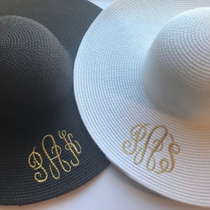 K&ouml;nnte beinhalten: Zwei Sonnenh&uuml;te, einer schwarz und einer wei&szlig;, mit goldenen Stickinitialen. Der schwarze Hut hat die Initialen "J.F.S." und der wei&szlig;e Hut hat die Initialen "R.F.S."
