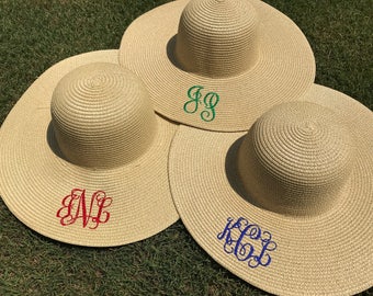 May include: Three straw sun hats with different colored monograms. The hats are beige and the monograms are green, red, and blue.