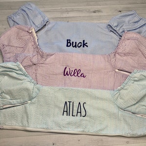 May include: Three striped fabric bibs with personalized names: Buck, Willa, and Atlas. The bibs are light blue, pink, and green.