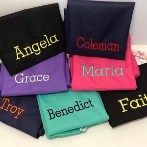 May include: A stack of eight fabric squares with different colors and names embroidered on them in various colors. The names are Angela, Coleman, Maria, Grace, Troy, Benedict, and Faith.