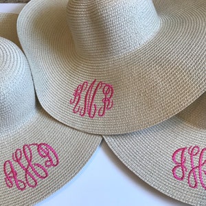 May include: Three straw sun hats with pink embroidered monograms. The monograms are "KCR", "AKG", and "JLL".