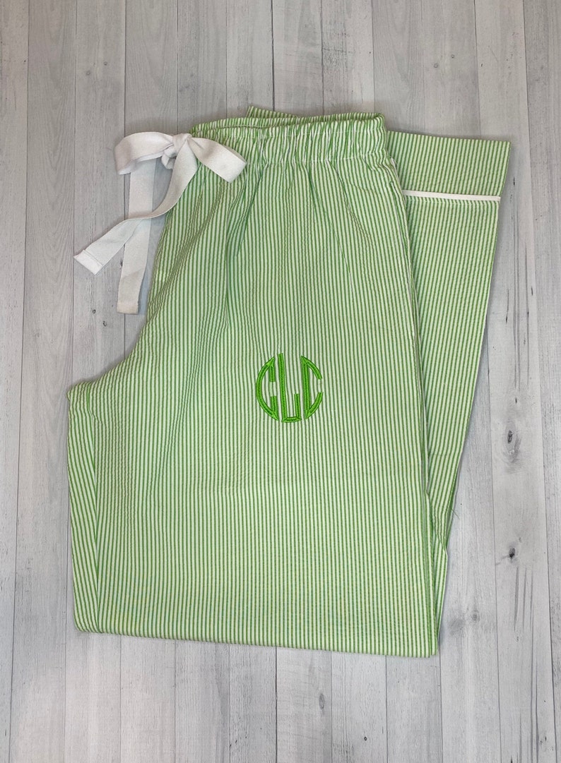 K&ouml;nnte beinhalten: Gr&uuml;n-wei&szlig;e gestreifte Schlafanzughose mit wei&szlig;em Kordelzug und einem gr&uuml;nen Monogramm "CLC" auf der Vorderseite.