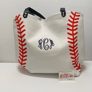 May include: White canvas tote bag with red baseball stitching and a navy blue monogram "KCM".
