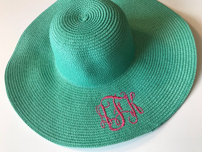 K&ouml;nnte beinhalten: Ein blaugr&uuml;ner Sonnenhut mit einem rosa gestickten Monogramm. Der Hut ist aus gewebtem Stroh.