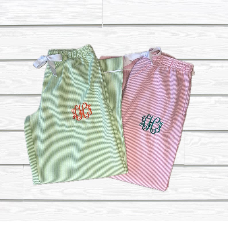 K&ouml;nnte beinhalten: Zwei Paar gestreifte Schlafanzug-Hosen mit Monogrammen. Ein Paar ist gr&uuml;n mit einem orangefarbenen Monogramm und das andere ist rosa mit einem gr&uuml;nen Monogramm.