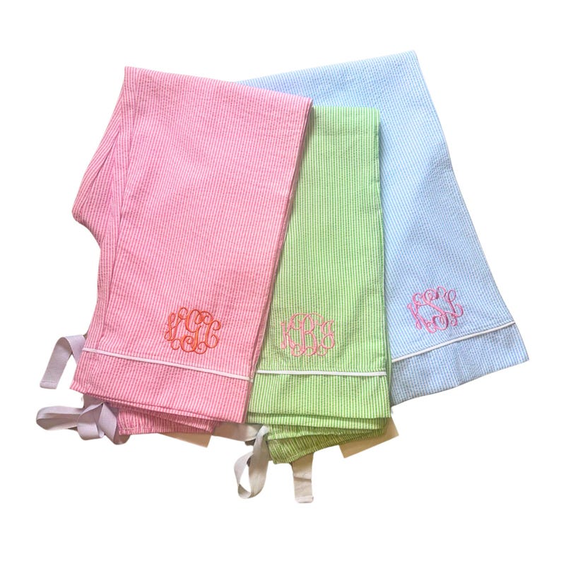 K&ouml;nnte beinhalten: Drei Paar gestreifte Pyjamas in Rosa, Gr&uuml;n und Blau mit wei&szlig;en Paspeln und gestickten Initialen.