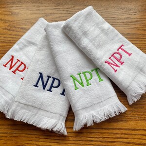 May include: Four white hand towels with fringed edges. Each towel has the letters "NPT" embroidered in a different color: red, navy blue, green, and pink.