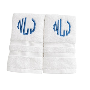 May include: Two white cotton towels featuring a blue embroidered monogram of the letters NL. Each towel has a textured surface with three horizontal ribbed bands near the bottom edge, providing a clean and simple design for bathroom use.