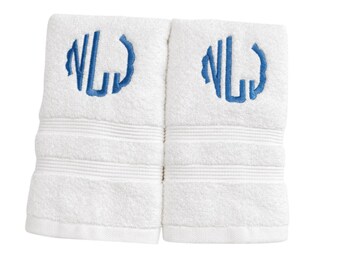 May include: Two white cotton towels featuring a blue embroidered monogram of the letters NL. Each towel has a textured surface with three horizontal ribbed bands near the bottom edge, providing a clean and simple design for bathroom use.