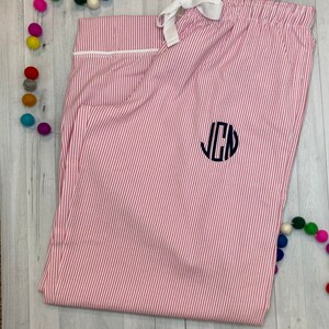 K&ouml;nnte beinhalten: Rosa-wei&szlig;e gestreifte Schlafanzughose mit wei&szlig;em Kordelzug und einem schwarzen Monogramm der Buchstaben "JCN" auf der Vorderseite.