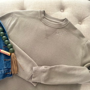 May include: A light brown sweatshirt with a crew neck and long sleeves. The sweatshirt has the word "d.m.n." embroidered on the front.