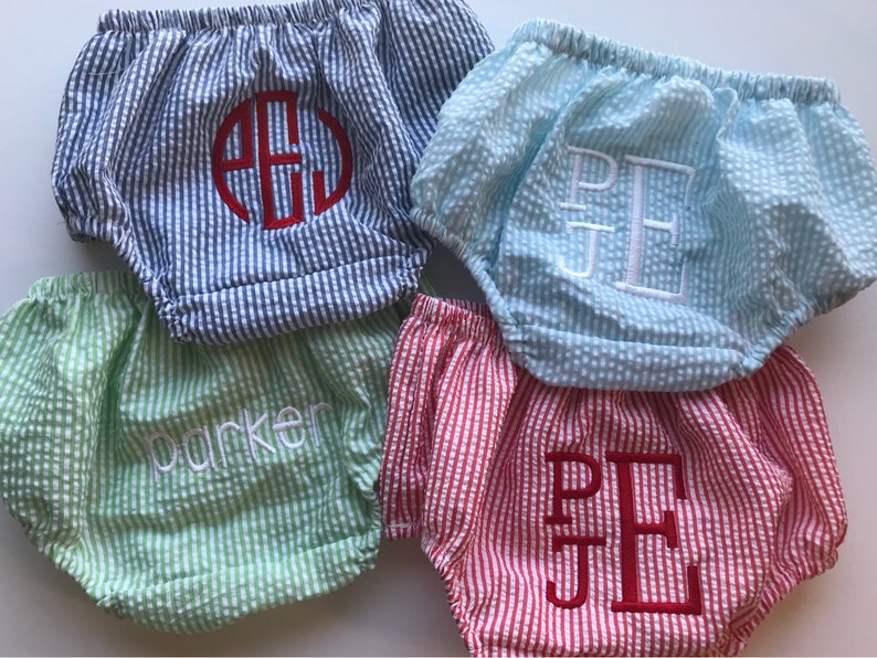 May include: Four pairs of baby bloomers in different colors and patterns. The bloomers are made of a soft, lightweight fabric and have a ruffled elastic waistband. The bloomers are embroidered with different names, including "Parker" and "P.E.J."