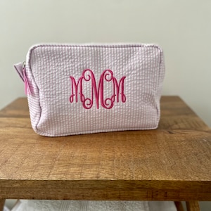 May include: A pale pink quilted makeup bag with a pink monogram that reads "MCM".