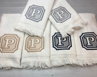 May include: A collection of white terry cloth towels featuring fringed edges and embroidered monograms. Each towel displays a letter P centered within a decorative frame, with embroidery thread colors including grey, gold, and dark navy blue.