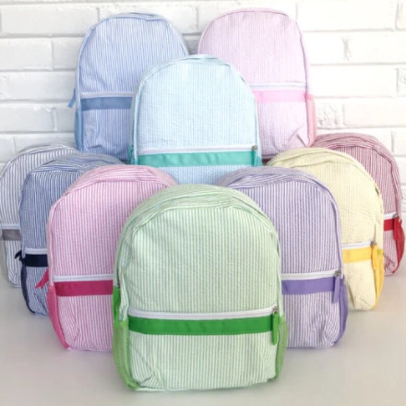 May include: A collection of nine striped backpacks in various colors, including light blue, pink, green, yellow, and purple. Each backpack has a contrasting colored zipper and a single strap.