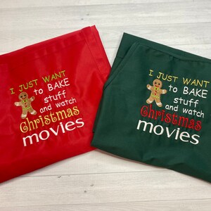 May include: Red and green aprons with the embroidered text "I JUST WANT to BAKE stuff and watch Christmas movies." Each apron features a gingerbread man graphic. The aprons are made of a smooth fabric.