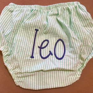 May include: Green and white striped baby bloomers with the name "Leo" embroidered in blue.