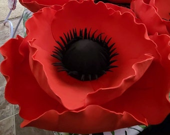 May include: A large, red, felt poppy flower with a black center. The flower is made of multiple layers of felt petals.