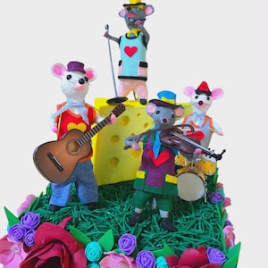 May include: A colourful diorama of a mouse band performing on a grassy stage with a cheese backdrop. The band members, in bright outfits, play a guitar, violin, and drums. The stage is decorated with vibrant flowers.