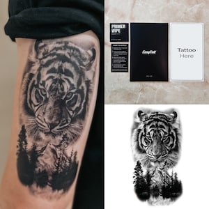 Puede incluir: Tatuaje temporal en blanco y negro de la cara de un tigre con una escena de bosque en la parte inferior. Incluye una toallita de imprimación, una tarjeta de instrucciones negra y una tarjeta blanca que dice "Tattoo Here".