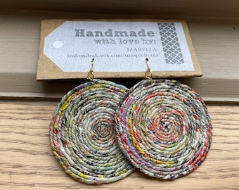 May include: Handmade paper earrings with a spiral design. The earrings are circular, with a gold-colored hook. The paper is multi-colored, with shades of red, yellow, green, and blue. The tag above the earrings reads "Handmade with love by: IZABELLA".