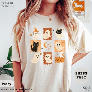 Pode incluir: Camiseta unissex marfim com ilustra&ccedil;&otilde;es de Halloween de fantasmas e gatos em molduras de selos postais. A camiseta inclui o texto "*Unisex T-Shirt*" e "Ivory". O design incorpora cores laranja, preto e branco.