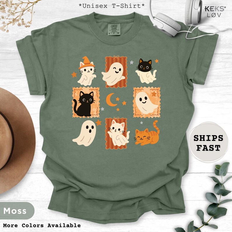 Pode incluir: Camiseta unissex verde musgo com um design tem&aacute;tico de Halloween. O design inclui gatos de desenho animado, fantasmas, estrelas e uma lua crescente. O texto "*Unisex T-Shirt*" est&aacute; no topo. A camisa tamb&eacute;m tem o texto "More Colors Available" e "KEKS L&Oslash;V".