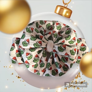 Peut inclure: Un nœud blanc avec un motif Grinch vert et rouge. Le nœud est fait d'un tissu doux et texturé.