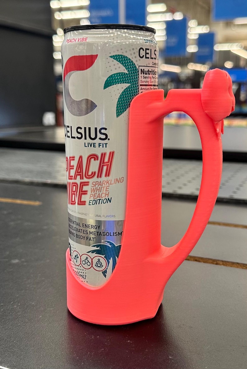 May include: A can of Celsius Peach Vibe sparkling white peach edition energy drink is held by a bright pink handle. The can has a white background with the Celsius logo and a palm tree design.