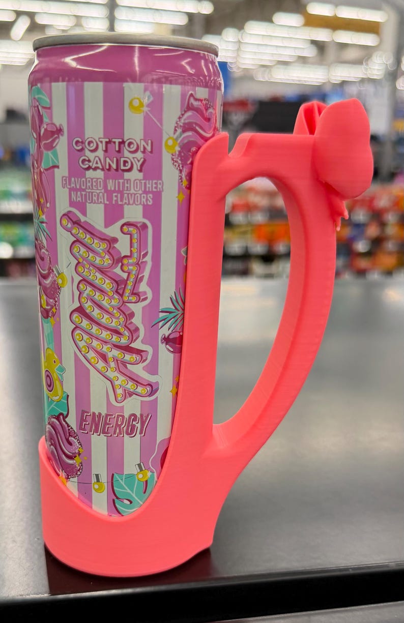 May include: A pink energy drink can with a matching pink handle. The can features a cotton candy design with the words "Cotton Candy" and "Energy". The handle has a bow detail at the top.