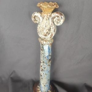 May include: A ceramic decorative pillar with a floral top and a blue and white column. The pillar has a round base and is approximately 30 cm tall. The top features a flower-like design with curled accents.