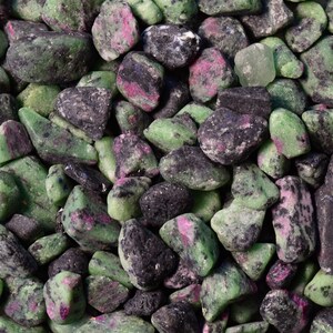May include: A close-up of a collection of green, black, and pink tumbled stones. The stones are smooth and have a variety of shapes and sizes.
