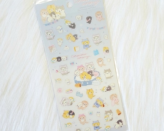 May include: A sheet of stickers featuring adorable cartoon cats wearing pajamas and holding various items. The stickers are on a light blue background with white stars and the text "Crococoro coronya" in a light blue font.