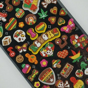 Op de afbeelding: Een vel met kleurrijke stickers met een reggae-thema. De stickers bevatten harten, schedels, vlinders, muzieknoten en de woorden "I Love Reggae".