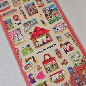 May include: A sheet of colorful stickers with a variety of illustrations. The stickers feature images of houses, characters, and the text "funny! funny!". The stickers are in a variety of shapes and sizes, and are on a red background.