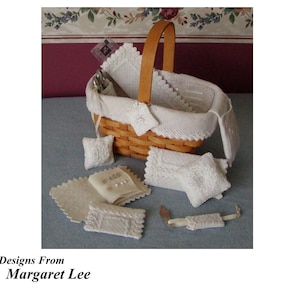 Può includere: Un cesto di vimini bianco pieno di oggetti ricamati bianchi, tra cui cuscini, un libro e una piccola borsa. Il cesto è appoggiato su una superficie blu chiaro.