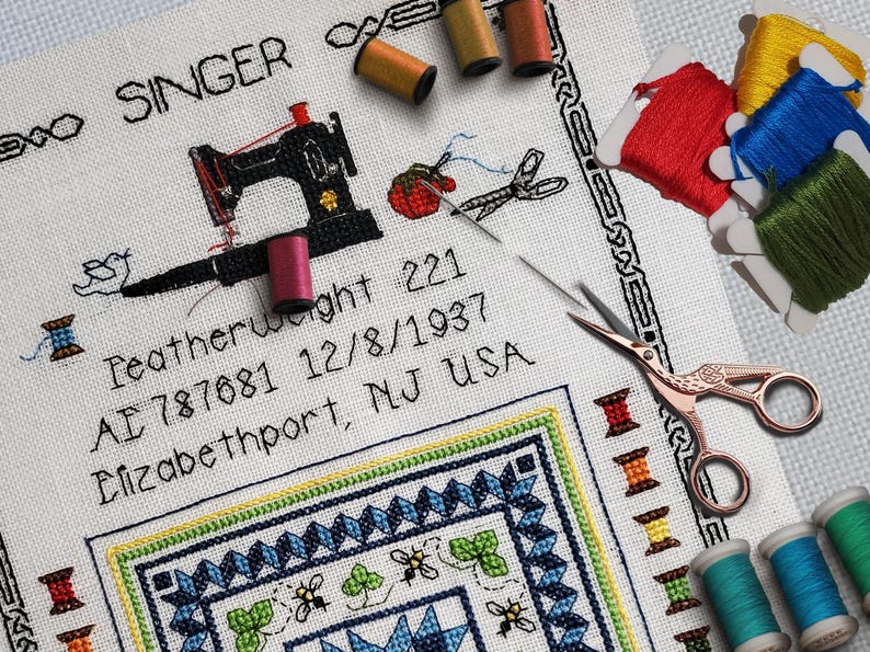 May include: A detailed cross-stitch design featuring a black sewing machine, spools of thread, and scissors. The text includes "SINGER" and other details. Various colored threads and a needle are also present.