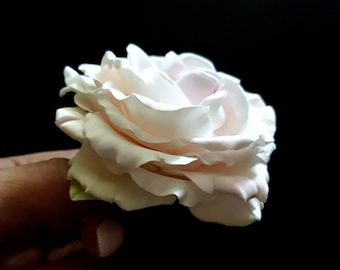 May include: A single, delicate, pale pink rose with a white center, crafted from fondant. The rose is held in a hand with manicured nails.