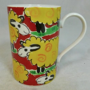 May include: A tall ceramic mug with a white handle, decorated with a sheep pattern. The mug has yellow sheep with black legs and faces on a red background, with green grass accents.
