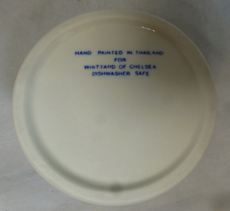 May include: White ceramic bowl with blue text that reads "Hand painted in Thailand for Whittard of Chelsea Dishwasher Safe".