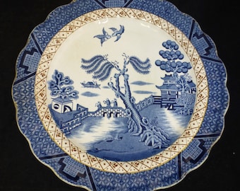 May include: A blue and white ceramic plate with a willow pattern design. The plate has a scalloped edge and a gold trim.